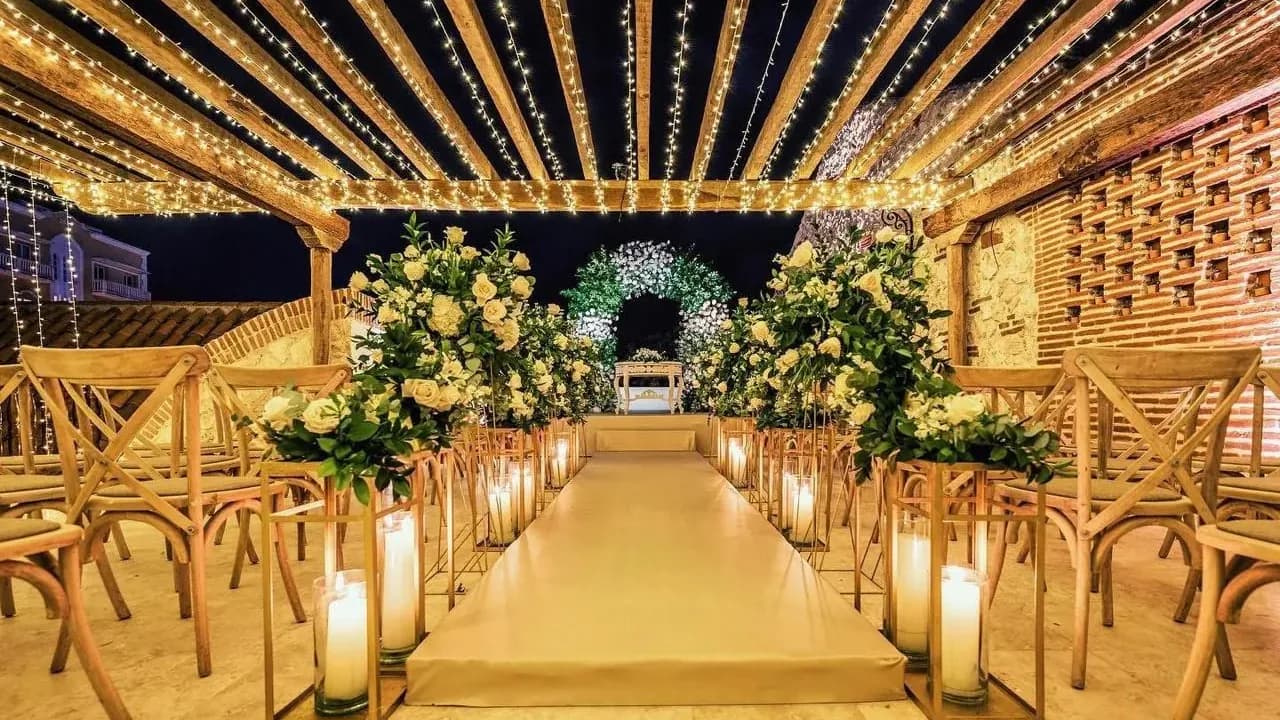 Pasillo de ceremonia con velas bajo una pérgola de luces y arcos de flores blancas, en una casa colonial de Cartagena.