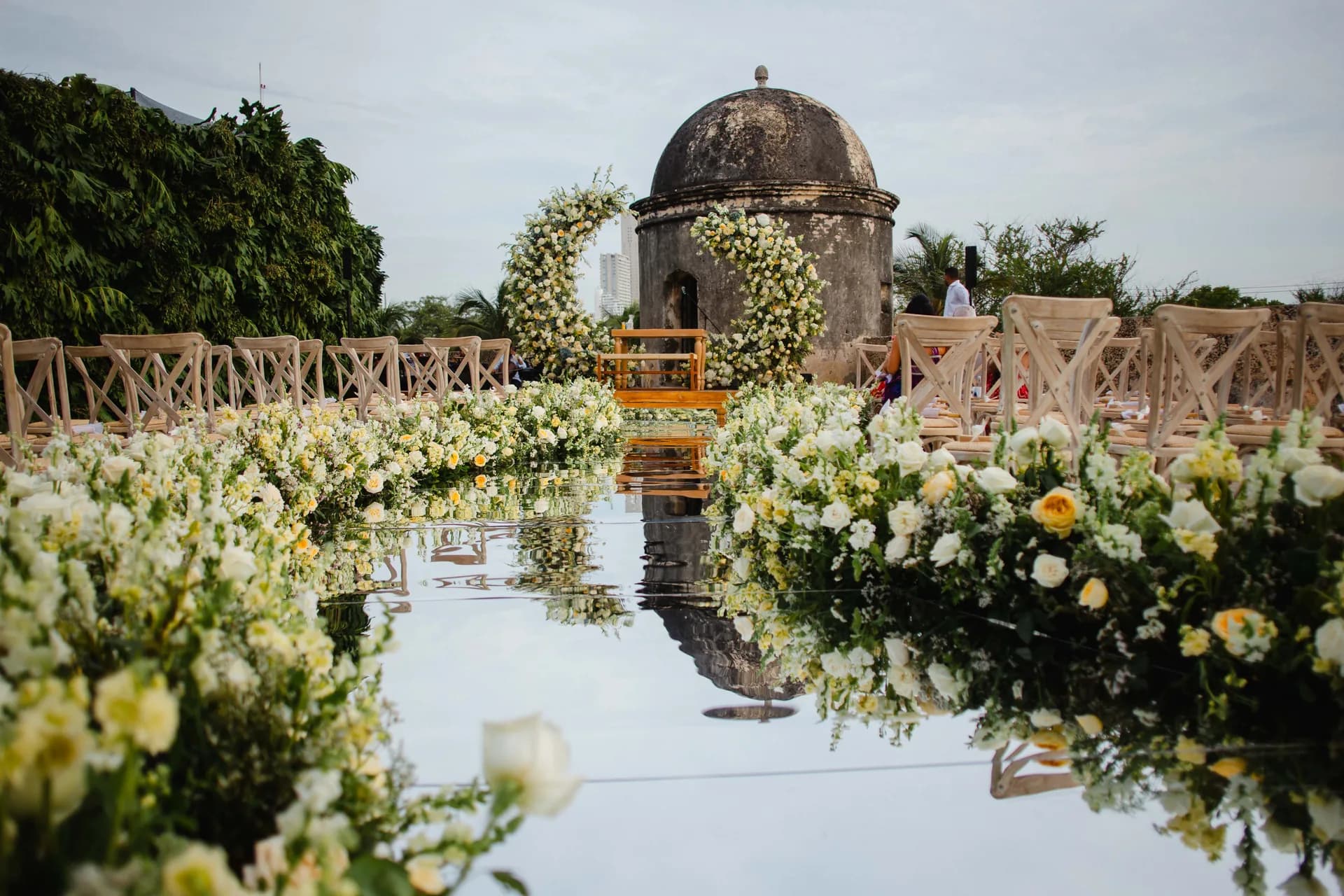 Pasillo de ceremonia con camino de espejo y arco de flores frente a una garita de la muralla de Cartagena