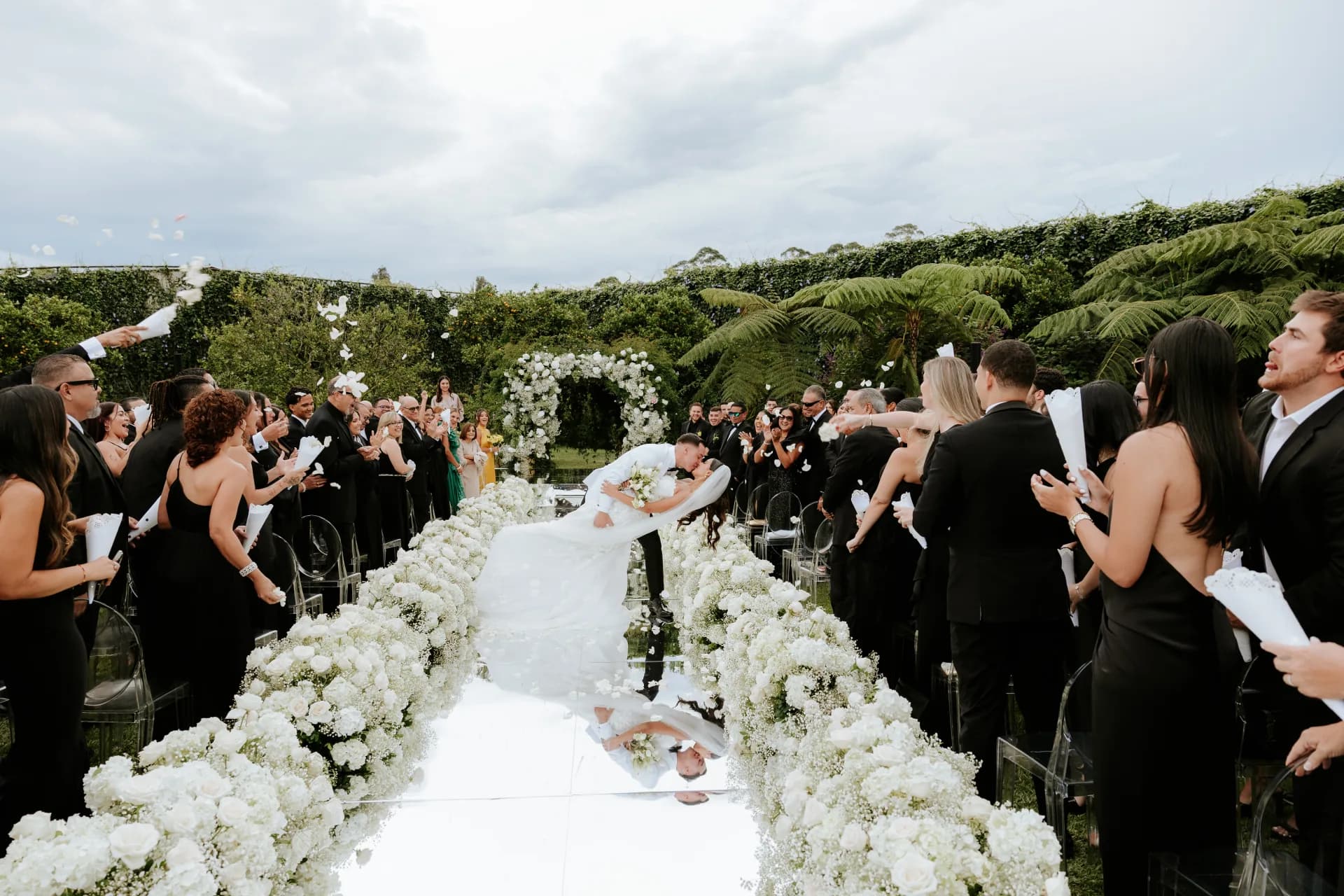 Los novios se besan al final del camino nupcial mientras los invitados lanzan pétalos